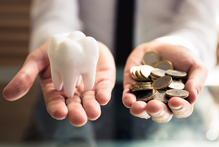 Person with money in one hand and a large tooth in the other hand