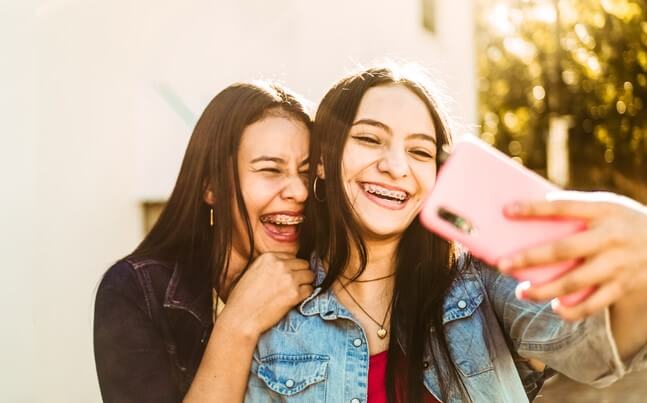 two young ladies wearing braces smiling and taking a selfie picture